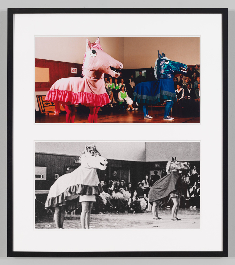 A framed photograph of two people in oversized horse costumes with skirts, one pink and one blue, performing in front of an audience. Below is a smaller black and white version of the same image.