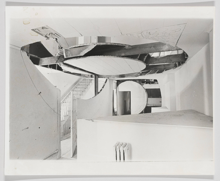 A black and white photograph showing an interior view of a modern architectural structure with a spiral staircase and curved elements. The image appears to be of a model or a partially constructed building, with visible damage or wear on the photograph itself.