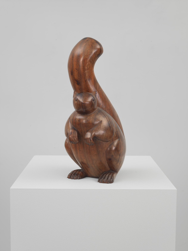A wooden sculpture of a stylized kangaroo with a joey in its pouch, displayed on a white pedestal against a light grey background.