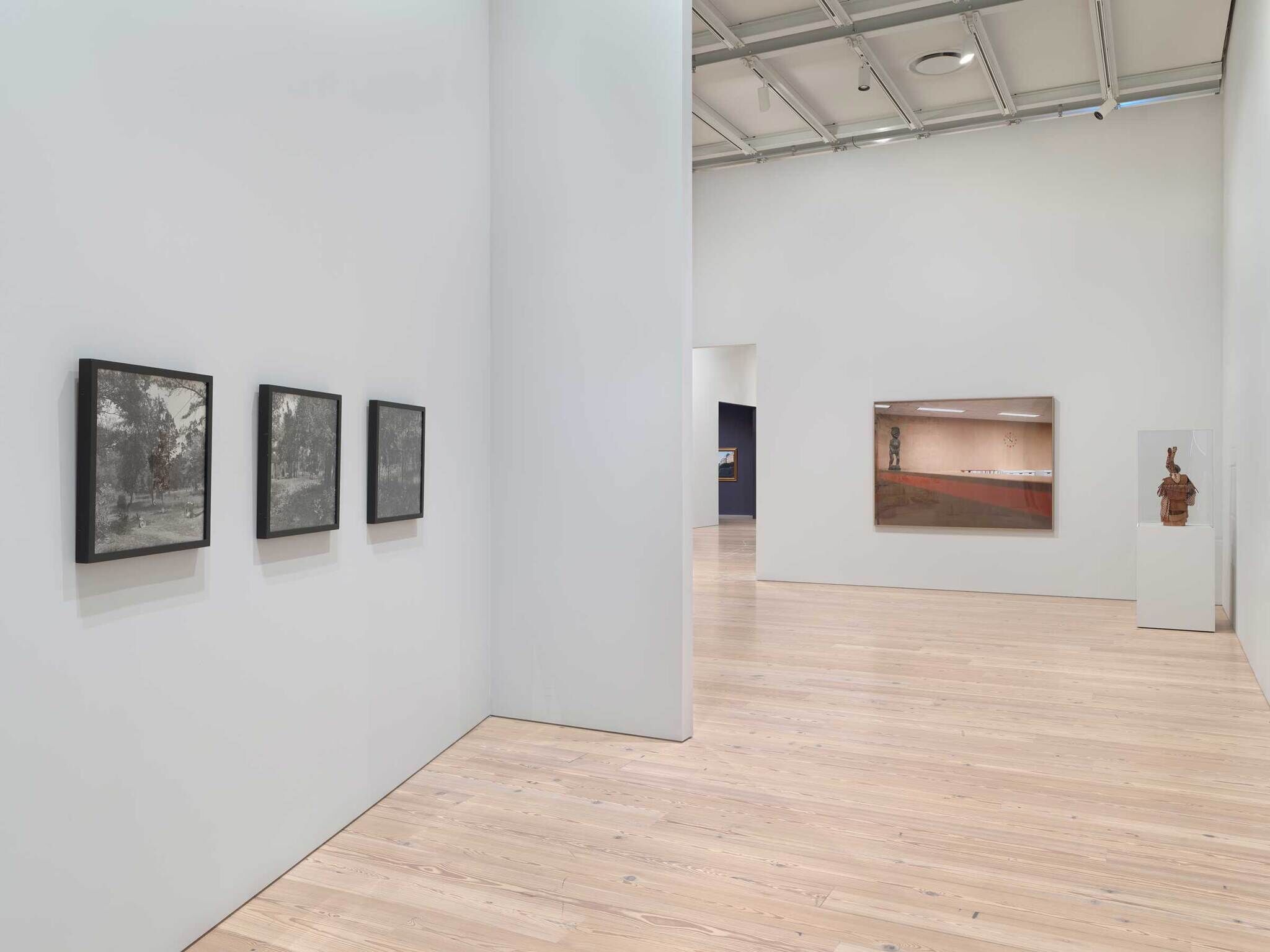 Three black and white framed photographs on the left and a sculpture in a case next to a larger painting.